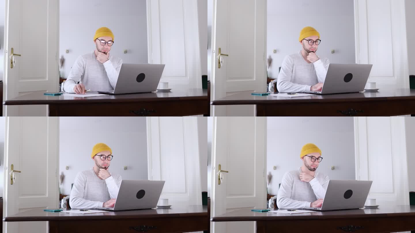 戴着眼镜、留着胡子的年轻白人男子正在用笔记本电脑写文件。远程工作，自由职业者和在线人力资源的概念