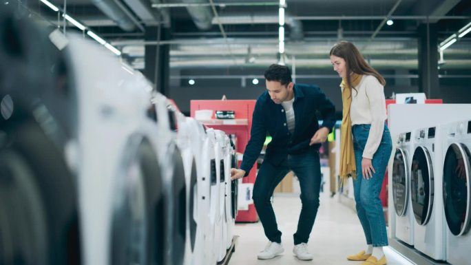 时尚青年男女在家用电器零售商店购买洗衣机。一对夫妇为他们的家选择洗衣清洁设备。顾客评价现代商店的选择