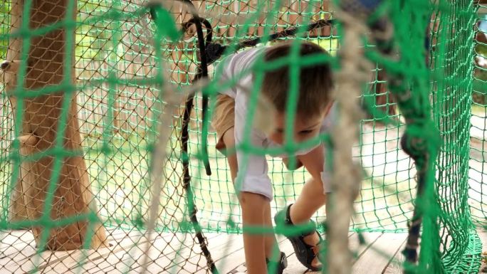在极限冒险公园里，小男孩爬过绳索和网。孩子们在户外玩耍，孩子们玩得开心，暑假和假期