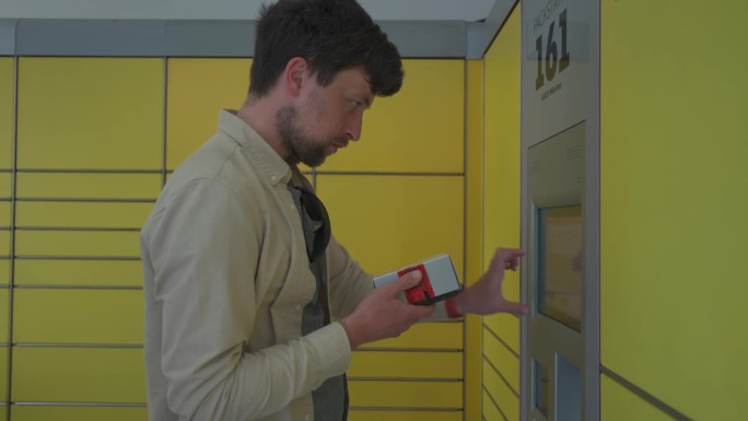 男子用黄色包装站自助送包裹。德国包裹和快递服务终端。寄件人在德国的黄色包装中心键入跟踪标签并发送包裹