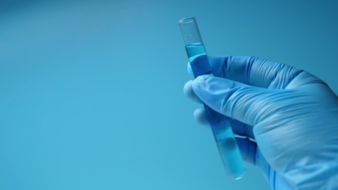 手戴蓝色手套，手持实验室测试玻璃管。蓝色的基调