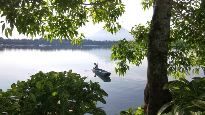 面目全非的湖上船夫操纵着他的木排船渡过湖面。树遮住了视野。模糊了