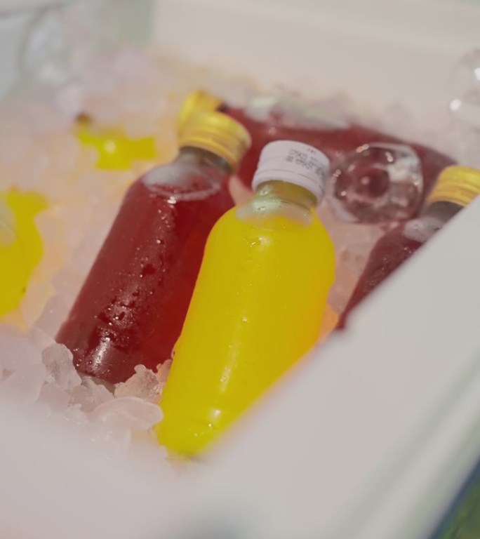 高视角，特写:一个人的手从冰桶里拿起两瓶矿物能量饮料，红色和黄色，在足球场旁边