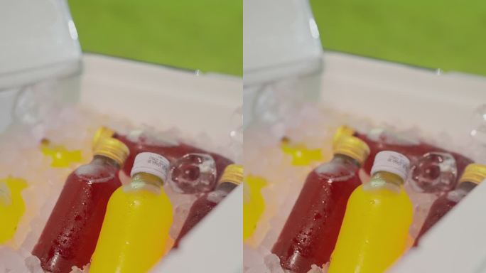 高视角，特写:一个人的手从冰桶里拿起两瓶矿物能量饮料，红色和黄色，在足球场旁边