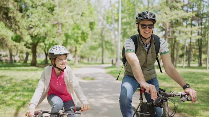 阳光明媚的一天，父亲和女儿在公园里骑自行车