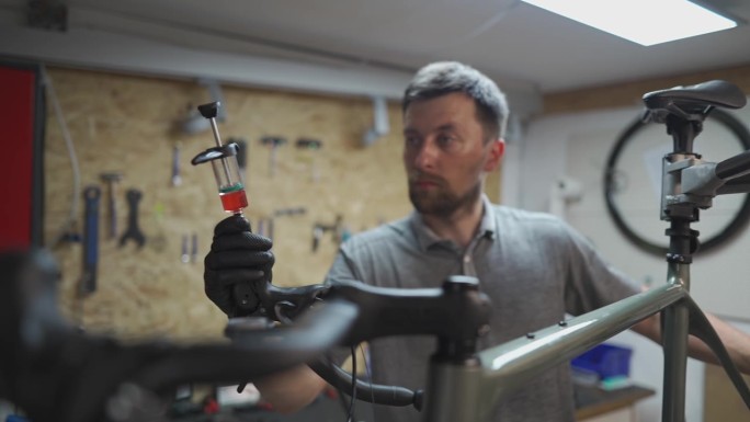 在刹车流血过程中，自行车修理工拿着装有刹车液的注射器。自行车修理工在车间给自行车的液压制动器注入制动