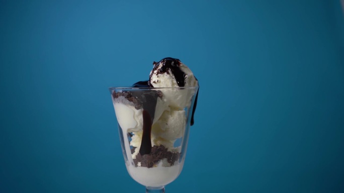 将巧克力糖浆倒入鲜奶油中，淋上蓝色背景的冰淇淋。冰淇淋广告。餐厅里美味的冰淇淋