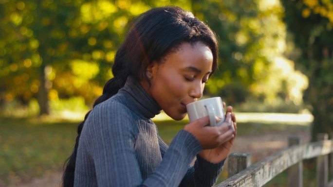 倚在秋野篱笆上微笑的女人喝着一杯咖啡