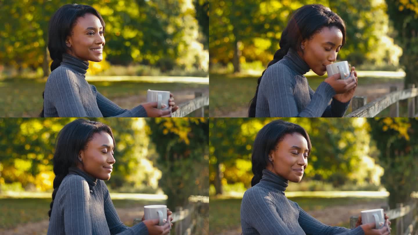 倚在秋野篱笆上微笑的女人喝着一杯咖啡