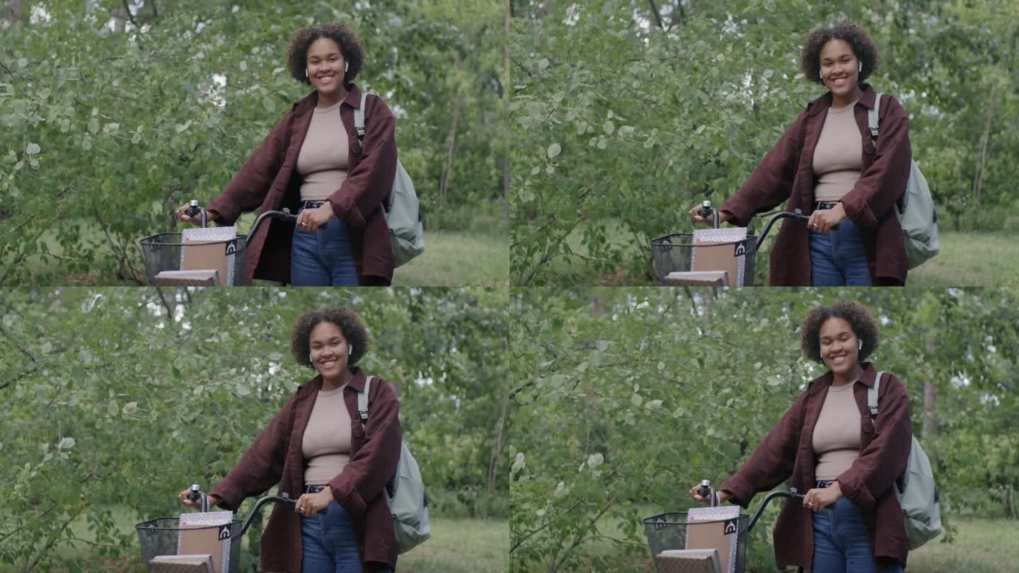 悠闲的非裔美国妇女站在绿色公园拿着自行车微笑的慢动作肖像