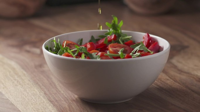 用橄榄油调味的慢动作，用芝麻菜，圣女果和红辣椒在碗里拌新鲜沙拉