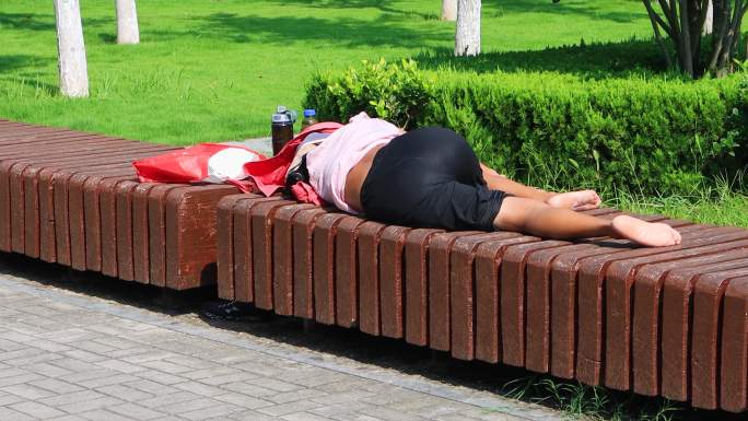 阳光下躺在公园长凳上衣服盖住头部的妇女