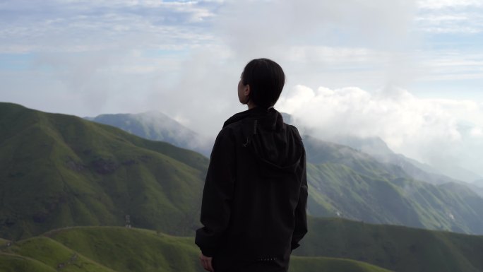 女性青年站在山顶看风景背影看远山感受自然