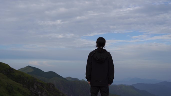 女性青年站在山顶看风景背影看远山感受自然