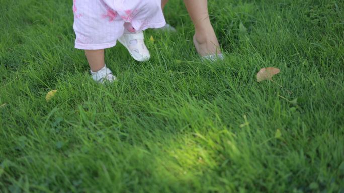 妈妈牵着孩子在草地学习走路