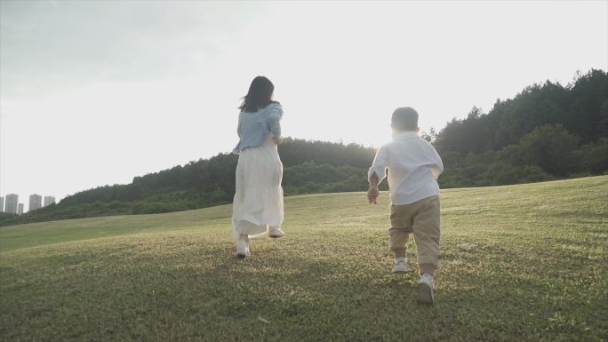 年轻妈妈陪伴小孩草地奔跑儿童节温馨家庭