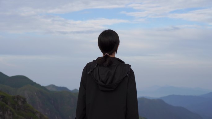 女性青年站在山顶看风景背影看远山感受自然