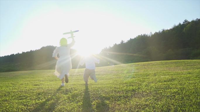 拿着飞机模型草地奔跑母子背影妈妈陪伴孩子