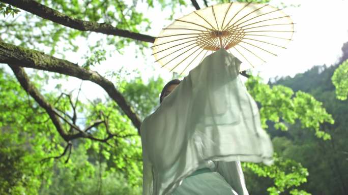 古装女生撑着油纸伞在树林中跳舞