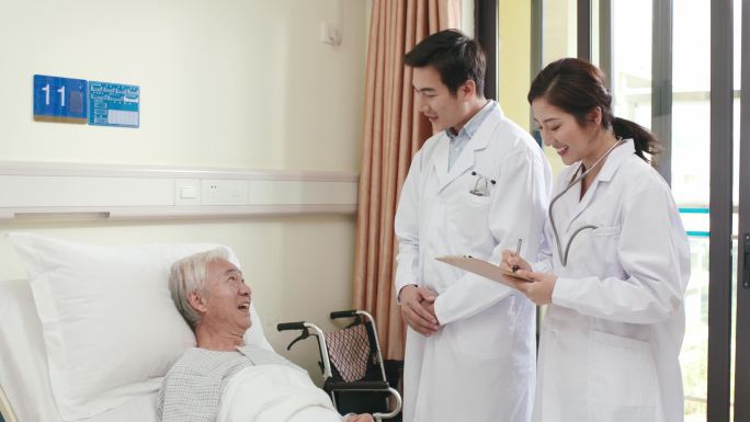 两名年轻的亚洲医生在医院病房里巡视老年病人
