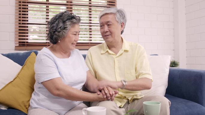 亚裔老夫妇手牵手，一边在客厅里，夫妻俩心情愉快，互相支持，躺在家里的病床上。生活方式 家庭老年家庭概