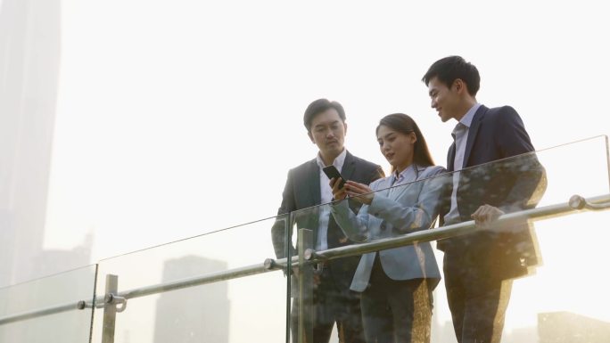 由三位亚洲企业高管组成的团队在户外用手机讨论业务
