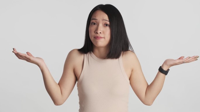年轻的亚洲女人看起来严肃地举起手对着被白色背景隔离的相机。我不知道怎么说