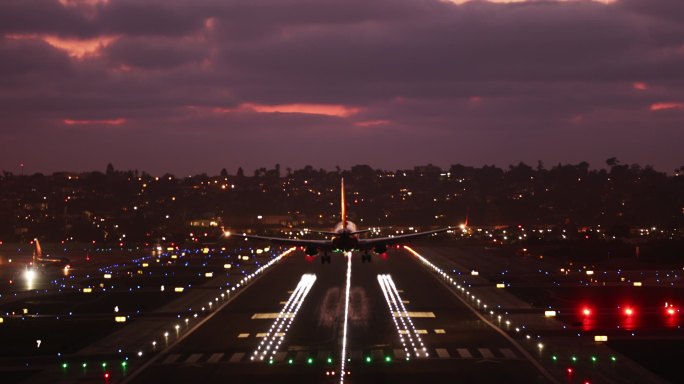 粉红色日落时的机场镜头。飞机降落与粉红色的日落天空背景