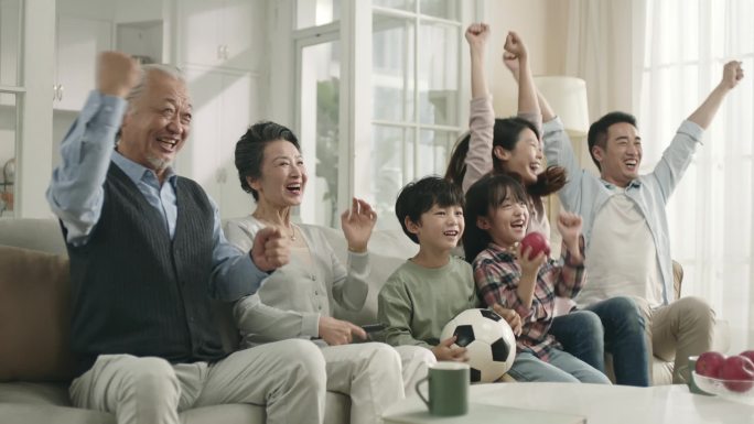 亚洲三代家庭坐在家里的沙发上观看足球比赛的直播一起庆祝进球