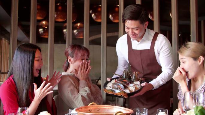 快乐的侍者带着火锅和海鲜在餐馆里招待一群朋友.
