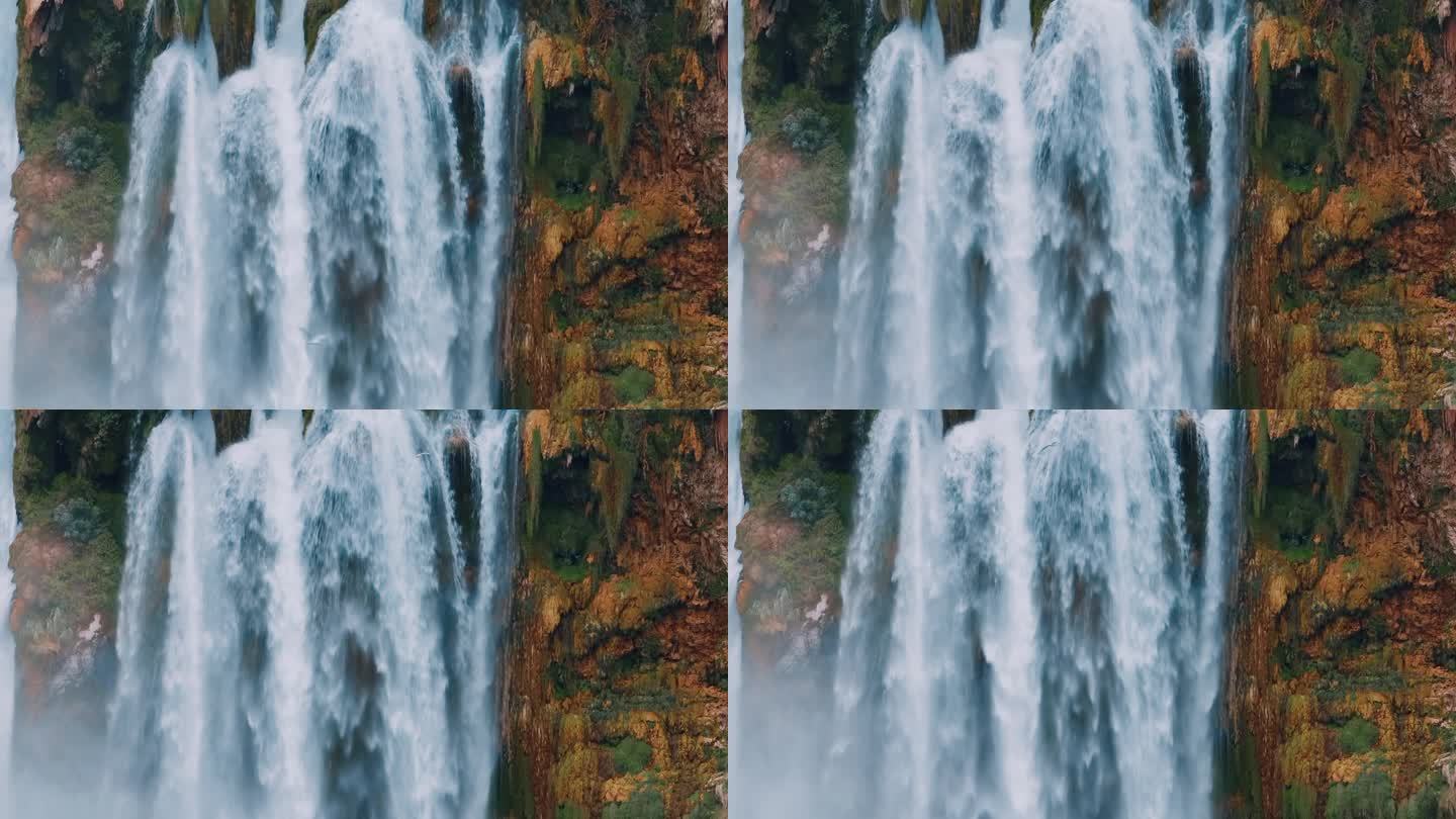 一个天然瀑布特写的无人机视频镜头。喷剂。泡沫。岩石上的绿色植被。自然因素。一只鸟飞过瀑布.高质量的镜