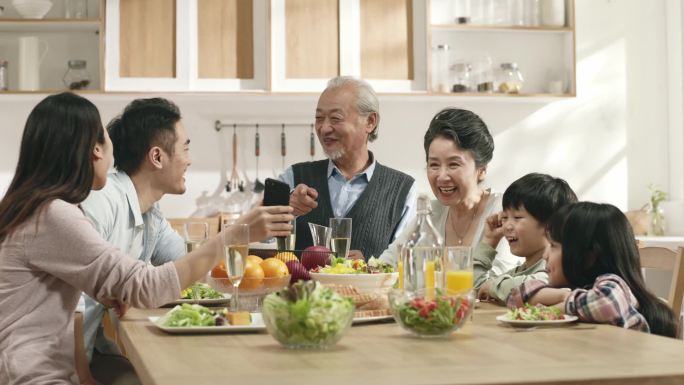 三代亚洲人快乐的家庭，一边在家里吃饭一边享受时光