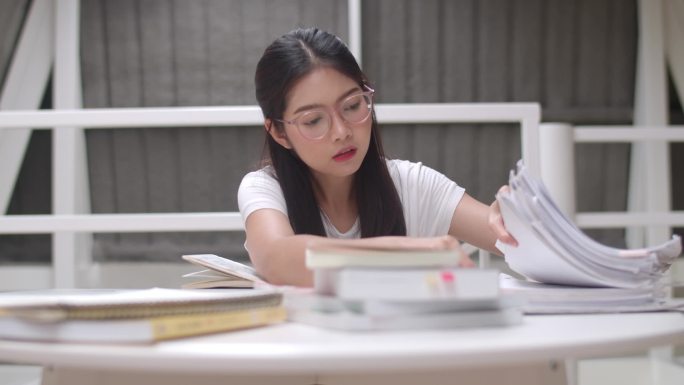 亚洲学生妇女读图书馆的书籍在大学。年轻的本科生女孩做家庭作业，读课本，努力学习知识和教育在课桌在大学