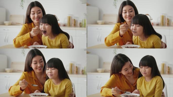 早上在家里的例行公事可爱可爱的亚裔母亲坐在厨房里，用牛奶和麦片喂女儿