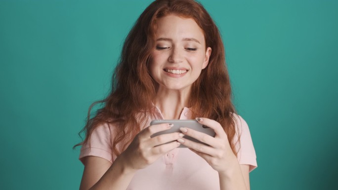 非常兴奋的红头发女孩快乐地在智能手机上玩着五颜六色的游戏