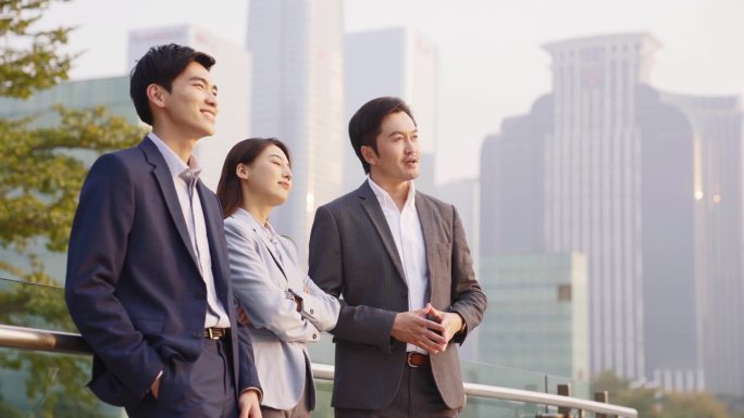 由三位亚洲商人组成的团队站在室外与现代城市天际线进行背景对话