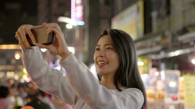 快乐的年轻亚洲女人在夜市用智能手机