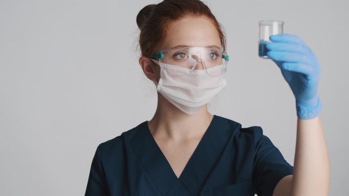 带防护眼镜、面罩和医用手套的专业女医生、与隔离的烧瓶一起工作