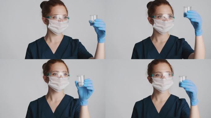 带防护眼镜、面罩和医用手套的专业女医生、与隔离的烧瓶一起工作