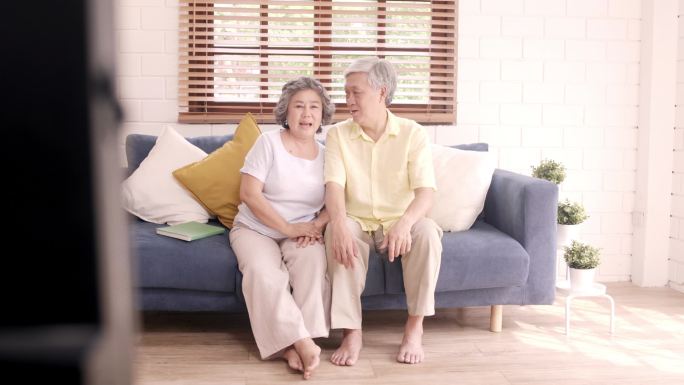 在家里客厅里看电视的一对亚洲老夫妻，在家里放松的时候，躺在沙发上享受爱情的时刻。享受家庭幸福的生活方