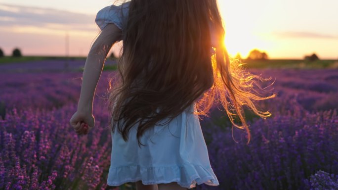 欢乐的女孩，美丽的女人在风景秀丽的日落时分在无尽的薰衣草田野中奔跑