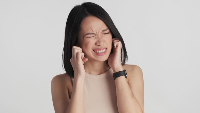 年轻的亚洲女人用手指捂住耳朵，因为它在白色背景上的声音太大了。我不想听