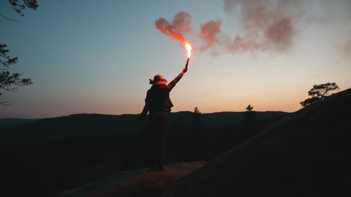 一个年轻的女人站在悬崖边上，在夜里挥动着照明弹。在山上远足。