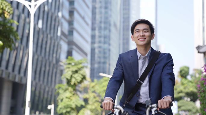 年轻的亚洲商人骑自行车去现代城市的商业区工作