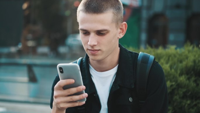 追踪学生在城市街道上使用智能手机享受无线网络通讯的照片。年轻学生放学后休息
