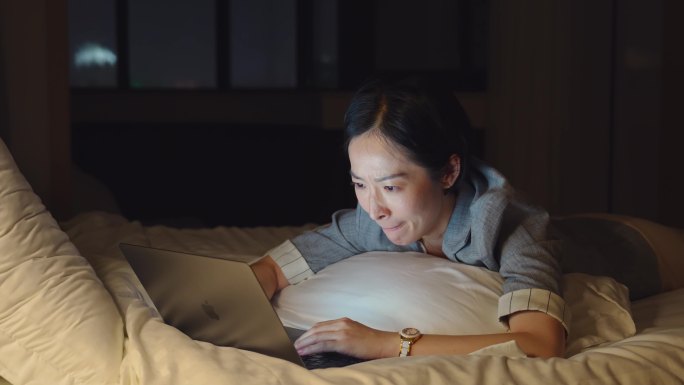 夜晚趴在床上用笔记本电脑工作的女白领