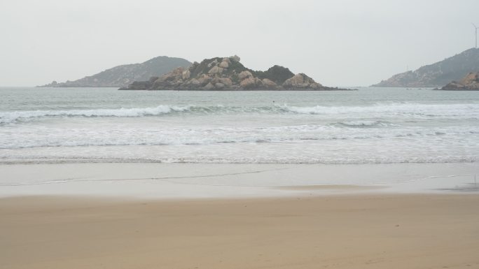 海浪涌上沙滩，远处的山依稀可见