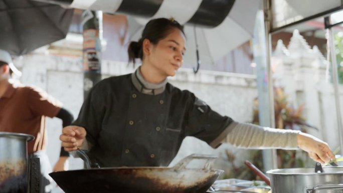 在曼谷市场，一位亚洲女厨师正在烹饪一种著名的泰国街头小吃——泰式炒粉。