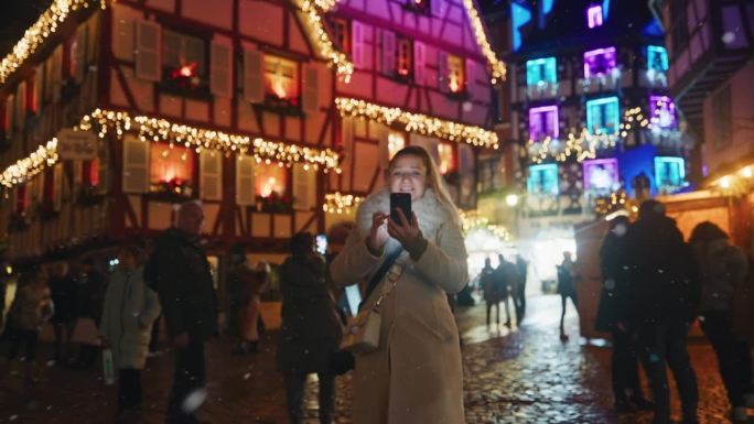 在科尔马欢快的圣诞气氛中，一名女子在下雪时使用她的智能手机