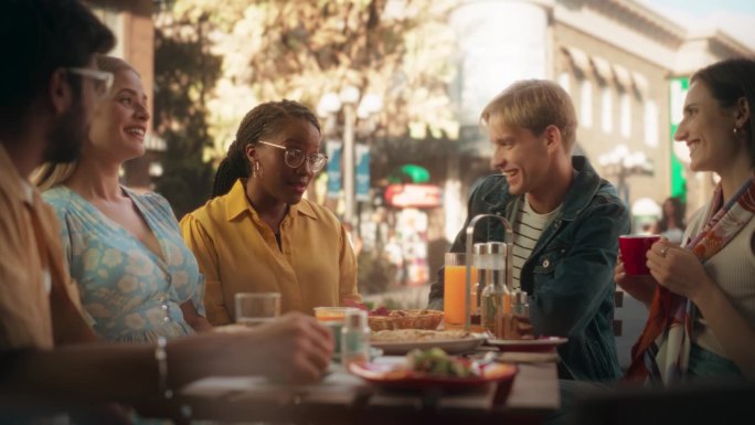 一群不同的朋友在街头咖啡馆享受休闲时光。年轻的女人和男人坐在桌子后面，有乐趣和快乐的谈话。非洲黑人女